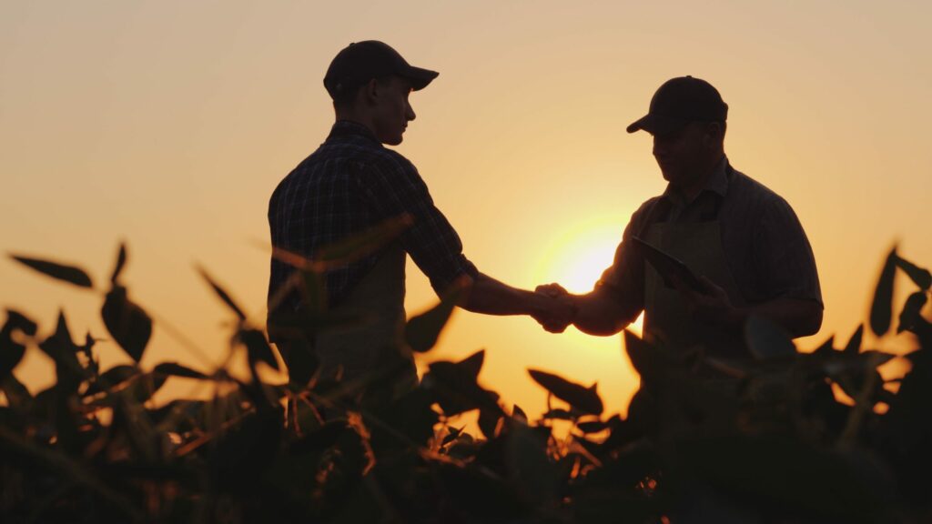 Two farmers talk on the field, then shake hands.