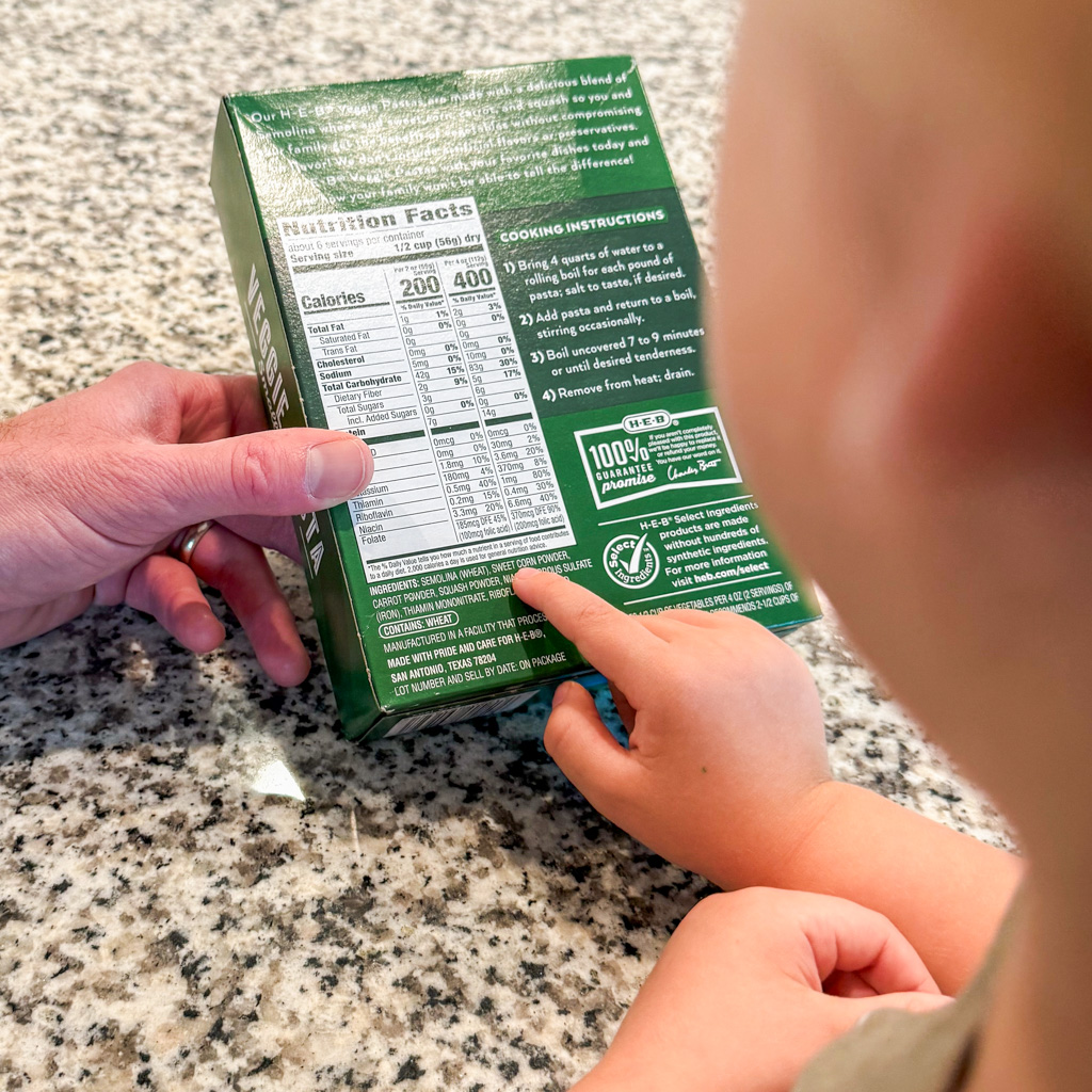 Small child and adult look at nutrition information on a noodles package.
